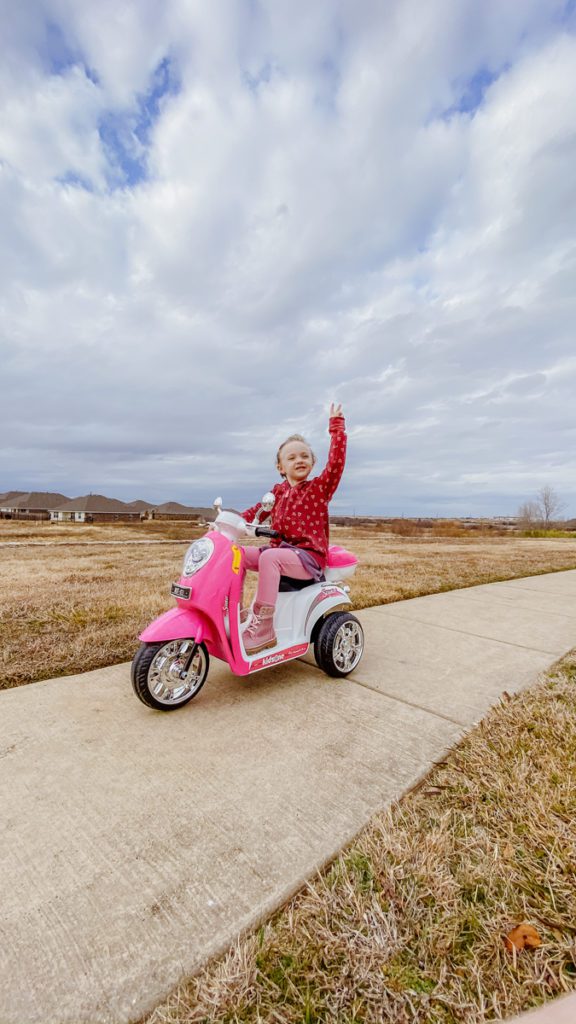 child on a pink scooter outside with clouds in the background