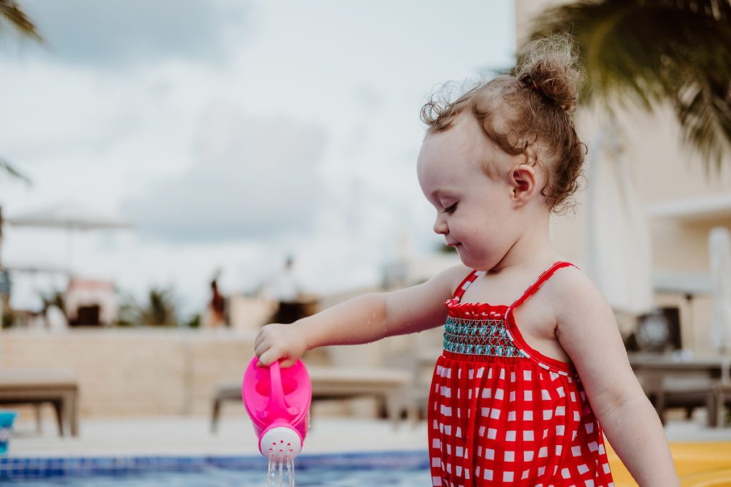 baby girl playing in the pool with a watering can