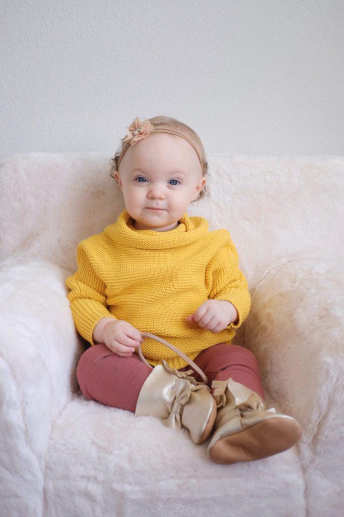 child in yellow sweater in front of a plain wall
