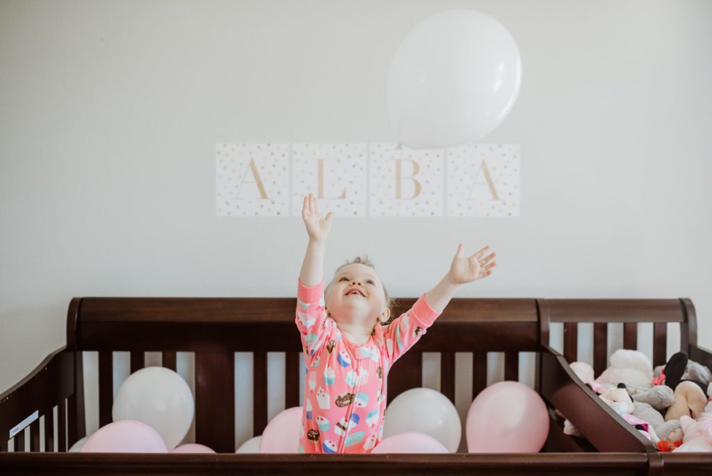 child in crib with pink balloons